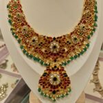 Traditional jadau kundan necklace featuring ruby red stones and green bead drops