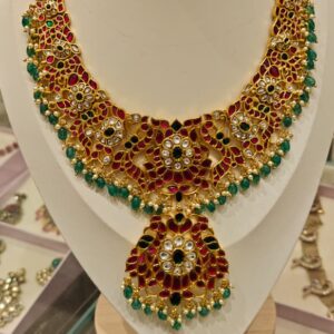 Traditional jadau kundan necklace featuring ruby red stones and green bead drops
